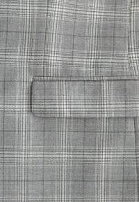 Tejido de cuadros gris con una textura tejida y líneas blancas que crean un patrón de cuadros. Incluye un detalle de un bolsillo en el pecho.