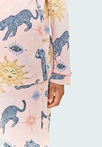Ljust rosa pyjamas-set med blå leoparder, sol och ögonmönster. Tillverkat av bomull med en avslappnad passform och kontrasterande muddar.