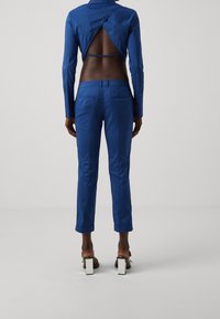 Niebieska skórzana kurtka z odkrytymi plecami, w komplecie z dopasowanymi niebieskimi spodniami. Gładka faktura, dopasowany krój oraz buty na kwadratowym obcasie.