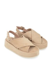 Sandales en suède beige avec un design croisé, bout ouvert et sangle à la cheville réglable, présentant une épaisse semelle compensée et une texture douce.