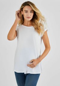 Top bianco a maniche corte con scollatura rotonda, realizzato in tessuto liscio, abbinato a jeans blu aderenti, evidenziando un fitting rilassato.
