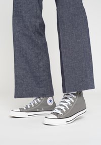Grijze hoge sneakers met witte rubberen zolen, contrasterende veters en een sterlogo als accent. Gecombineerd met losse, marineblauwe broeken.