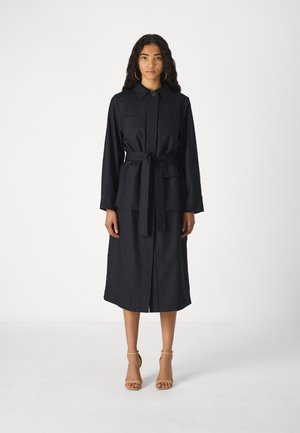 Navy pinstriped dress with a collar, front-button closure, tie waist, and two chest pockets, reaching mid-calf. Worn with nude heels.