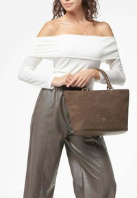 Borsa a tracolla in suede marrone con superficie testurizzata, forma rettangolare e manici corti. Abbinata a un top crema con spalle scoperte e pantaloni marroni.
