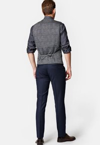 Szary i niebieski kamizelka w kratę, dopasowany krój, z paskiem w talii. Połączona z granatowymi spodniami slim fit i brązowymi butami. Szczegóły w teksturze tkaniny.
