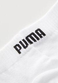 Hvite sokker med en tykk mansjett, med en svart brodert "PUMA"-logo. Materialet ser mykt ut med en strukturert overflate.