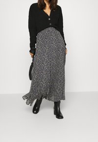 Cárdigan negro con botones sobre una falda maxi de flores oscuras con un dobladillo rizado, combinada con botas de tacón negras y un bolso negro.