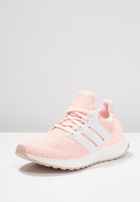 Jasnoróżowy but sportowy z teksturowanym, dzianinowym wierzchem, białym wzorem z trzema paskami, amortyzowaną podeszwą i gumową podeszwą zewnętrzną.