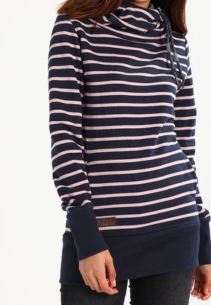 Femme portant un pull bleu marine à rayures horizontales rose clair, un col bénitier avec cordon de serrage, avec des poignets et un ourlet bleu marine.