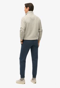 Grijze sweater met kraag en geribde manchetten, gecombineerd met marineblauwe sweatpants. Neutrale sneakers met beige accenten maken de outfit compleet.