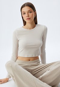 Vaalea beige lyhyt pitkähihais-toppi, jossa on ribbitekstuuri. Yhdistetty saman sävyisiin, pehmeätekstuurisiin, leveälahkeisiin housuihin.