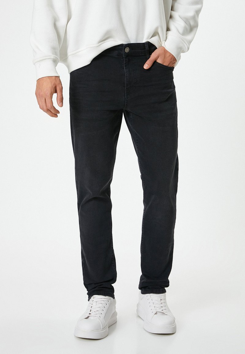 Jeans de mezclilla azul oscuro con un diseño ajustado, que presentan una textura sutil. Combinados con una sudadera blanca y zapatillas blancas.