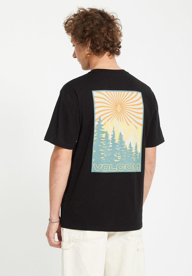 Sort bomulds T-shirt med en farverig grafik på ryggen, der viser bjerge, træer og solstråler. Brandnavnet "Volcom" er vist.