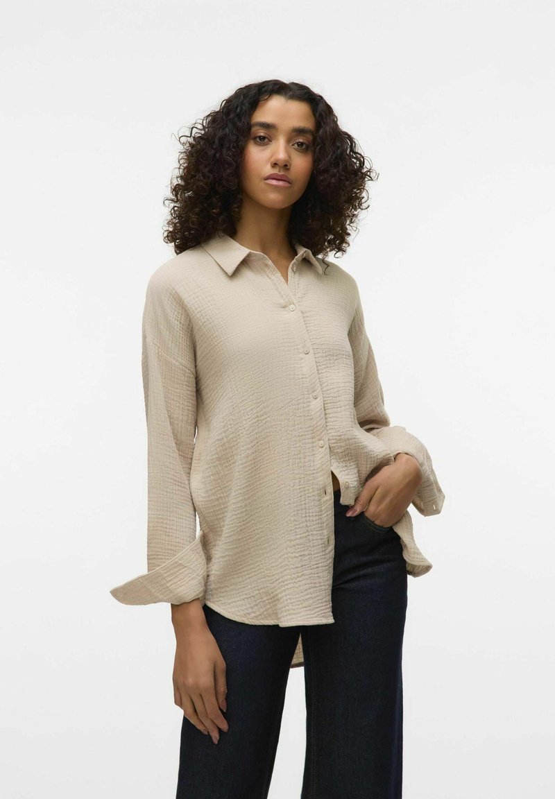 Beige, long-sleeved shirt with a textured fabric, collared neck, and button closure, paired with dark blue wide-leg jeans.