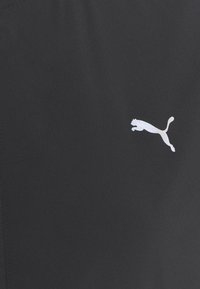 Tejido atlético negro con un sutil brillo, con un prominente logo blanco de Puma. Textura suave y diseño ajustado.