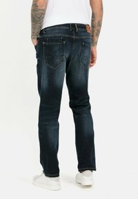 Mørkeblå denimbukser med en afslappet pasform, fem lommer og kontrastsyet, vist sammen med en hvid t-shirt og hvide sneakers.