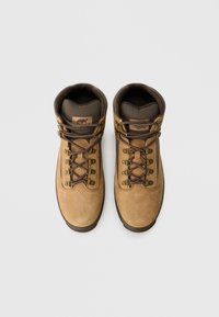 Stivali da trekking in pelle marrone con dettagli marrone scuro, occhielli metallici e lacci scuri. Suola robusta e colletto imbottito per il comfort.