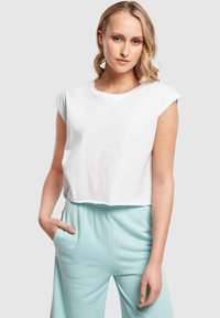 Bílý crop top z lehkého materiálu s kulatým výstřihem, krátkými rukávy a volným střihem, spárovaný se světle modrými kalhotami.