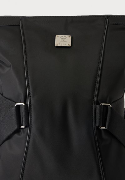 Sac à dos en nylon noir avec bretelles réglables et une petite plaque métallique rectangulaire estampillée MCM Munich G3231.
