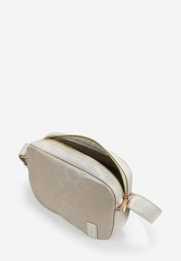 Bolso bandolera en faux cuero beige claro con un patrón sutil, herrajes en tono dorado y cierre de cremallera. Incluye una correa lateral para llevar.