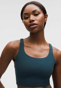 Vihreänsininen urheiluliivit, joissa on sileä pinta, leveät olkaimet ja pyöreä pääntie. Tukevan ja joustavan rakenteen ansiosta ne sopivat aktiiviseen käyttöön.