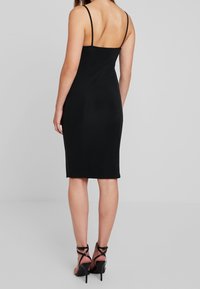 Schwarzes Bodycon-Kleid mit dünnen Trägern, knielang, glatte Textur, figurbetonte Silhouette, mit tiefem Rückenausschnitt und dezenten seitlichen Schlitzen.
