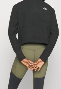 Schwarzer, verkürzter Sweatshirt mit geripptem Saum; olivgrüne Leggings mit einem Farbblockdesign und dunklen Akzenten sowie sichtbaren Nähten.
