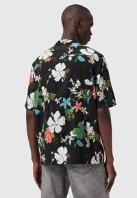 Czarna koszula z krótkim rękawem w kwiatowy wzór z dużymi, wielokolorowymi hibiskusami i liśćmi, o luźnym kroju i kołnierzyku typu camp.