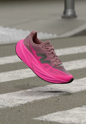 Løbesko med pink og gråt overmateriale og tyk neonpink sål svævende over et gråt asfaltfodgængerfelt med hvide striber.