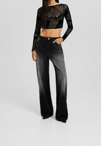 Czarny przezroczysty długi rękaw crop top z kwiatowym wzorem, w połączeniu z wysokim stanem spranym czarnym szerokim dżinsami. Obydwie części mają gładką teksturę.