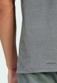 T-shirt gris en tissu doux, avec un col rond, des manches courtes et un petit logo "AEROREADY" près de l'ourlet.