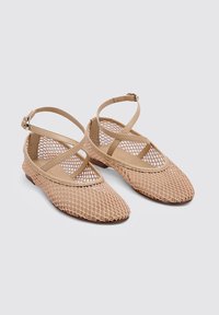 Ballerines en maille beige avec des sangles croisées, bout pointu, semelle plate et design en filet texturé. Style minimaliste avec un aspect ouvert.