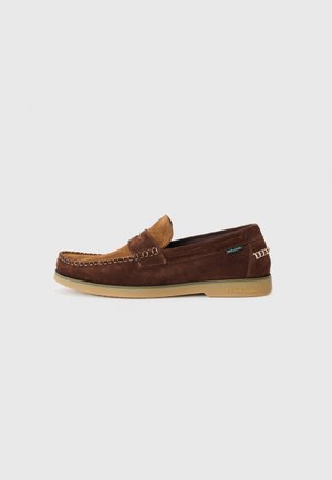 Mocassins en daim marron avec un accent en cuir tan, semelle en caoutchouc et couture décorative. Présente un design sans lacets et une marque en relief sur le côté.