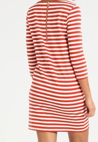 Czerwona i biała sukienka w paski z rękawami trzy czwarte, z zapięciem na zamek z tyłu, uszyta z miękkiego, elastycznego materiału.