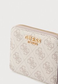 Bézs, texturált pénztárca cipzáras záródással, kiemelkedő monogram mintával és arany "GUESS EST 1981" logóval az elején.