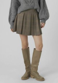 Bruin geruit geplooid minirok gecombineerd met een grijs textuurtrui en olijfgroene kniehoog boots. Eenvoudig, functioneel ontwerp.