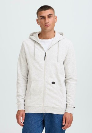 Haut de sweat à capuche zippé gris clair en tissu doux avec une poche avant, capuche à cordon et poignets côtelés, associé à un jean bleu.