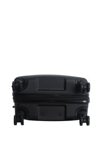 Black hard-shell suitcase lying flat showing four spinner wheels and closed zipper against a white background.