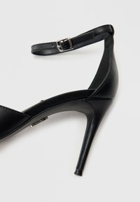 Schwarze High-Heel-Sandale mit elegantem Lederobermaterial, schmalem Knöchelriemen und spitzer Zehenpartie. Verfügt über einen Stiletto-Absatz und eine verstellbare Schnalle.