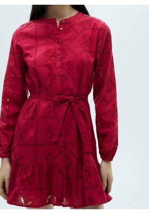 Mujer con un vestido rojo de manga larga con patrones florales recortados, botones en la parte delantera, un cinturón atado en la cintura y un dobladillo con volantes.