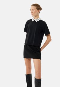 Top negro de manga corta con un collar blanco bordado y una falda negra a juego. El conjunto presenta un corte relajado y una textura suave.