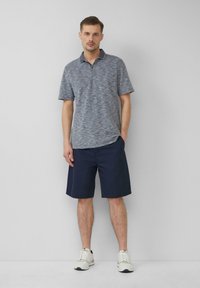 Blauwe polo met korte mouwen en een textuur, voorzien van een contrasterende kraag, gecombineerd met knielange marineblauwe shorts. Witte sneakers maken de look compleet.