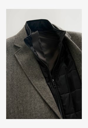 Brauner Blazer im Fischgrätmuster mit einem schwarzen gepolsterten Futter, das mit einem Reißverschluss geschlossen wird. Verfügt über einen taillierten Kragen und Revers und zeigt einen strukturierten Stoff.