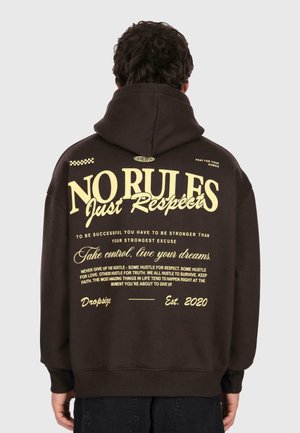 Personne portant un sweat à capuche noir avec du texte jaune au dos : "PAS DE RÈGLES Juste du Respect," phrases motivantes, et "Dropsiz Est. 2020."