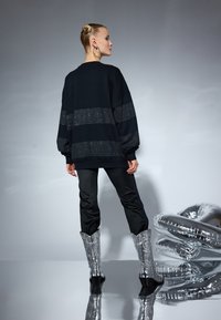 Felpa nera oversize con motivo a pois; abbinata a pantaloni neri slim e stivali da cowboy argentati lucidi, con finitura testurizzata.