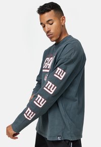 Pitkähihaisen puuvillapaidan tumman harmaan värin päällä on rohkeat valkoiset ja viininpunaiset "NY"-grafiikat hihoissa ja rinnassa. Paita on valmistettu teksturoidusta kankaasta ja siinä on rento istuvuus.