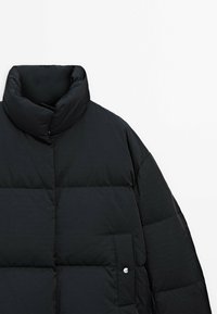 Black puffer jacket with a high collar, quilted texture, and side pocket featuring a button closure. Smooth, lightweight outer material.