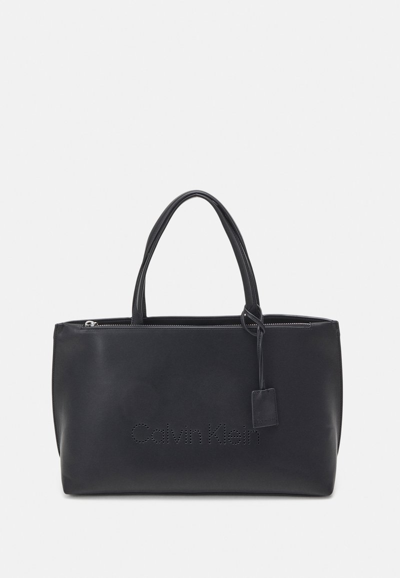 Sac cabas rectangulaire noir avec deux poignées, fermeture éclair et logo "Calvin Klein" perforé à l'avant.