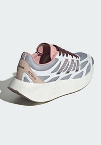 Scarpa sportiva grigia e bianca con parte superiore in mesh testurizzato, accenti rosa e una spessa suola bianca. Presenta un design a tre strisce e un marchio distintivo.