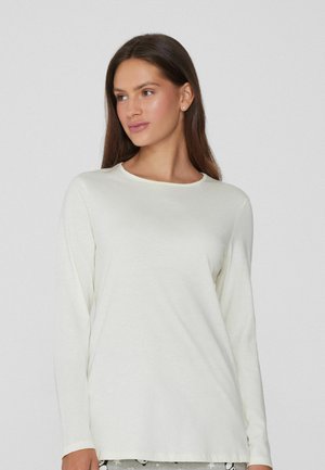 Blusa de manga larga de color crema, confeccionada en una tela suave y con un corte relajado, que presenta un sutil detalle de costura en las mangas.